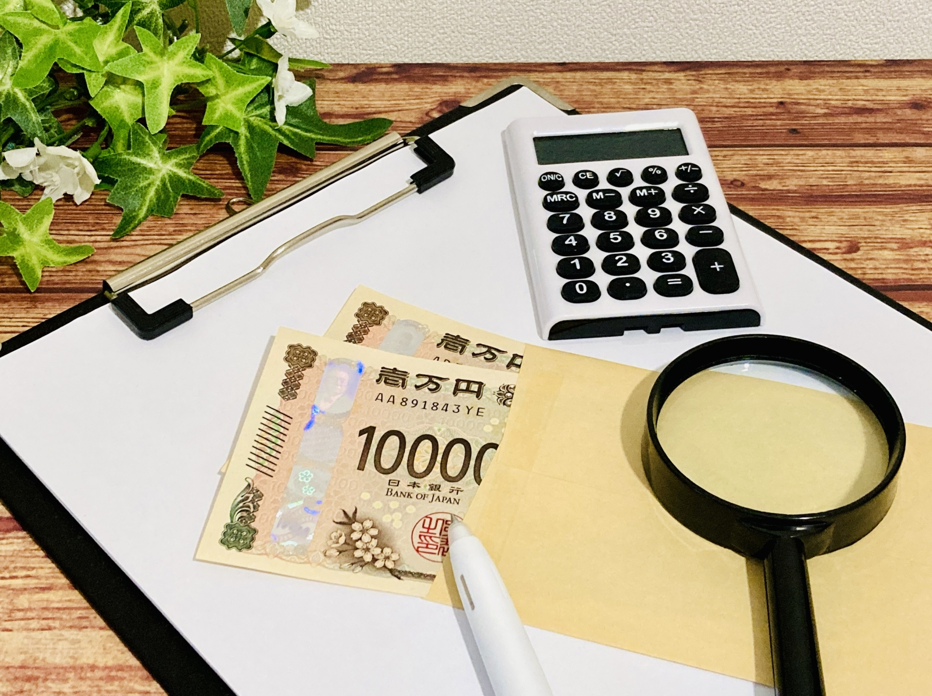 1万円札、電卓、虫眼鏡、クリップボードが置かれている