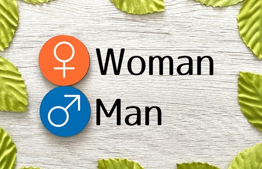女性と男性のシンボルマークと“Woman”“Man”の文字、背景に木目と緑の葉